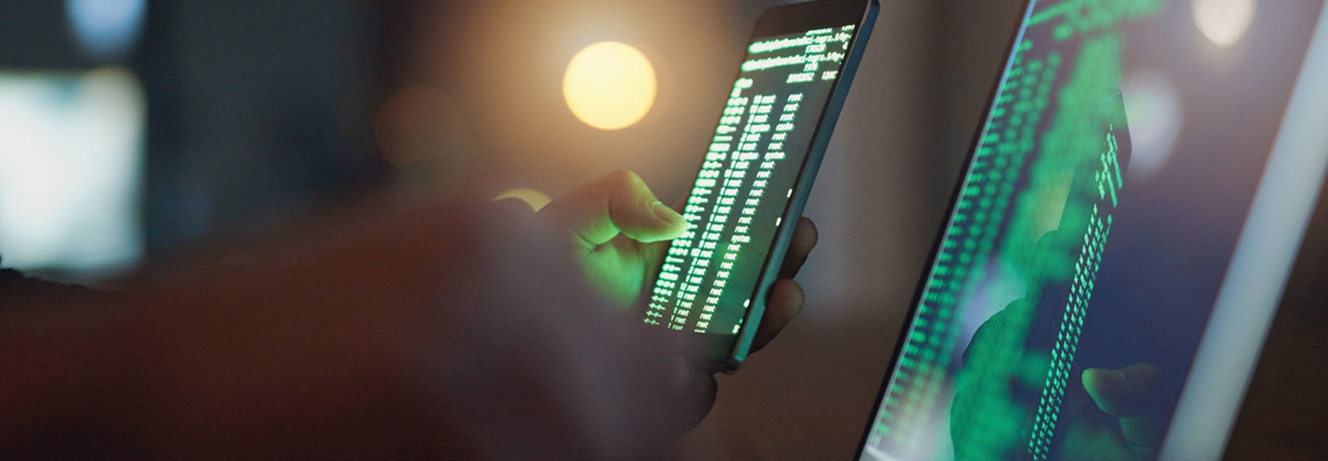 Shot of an unrecognizable hacker using a cellphone and laptop in the dark