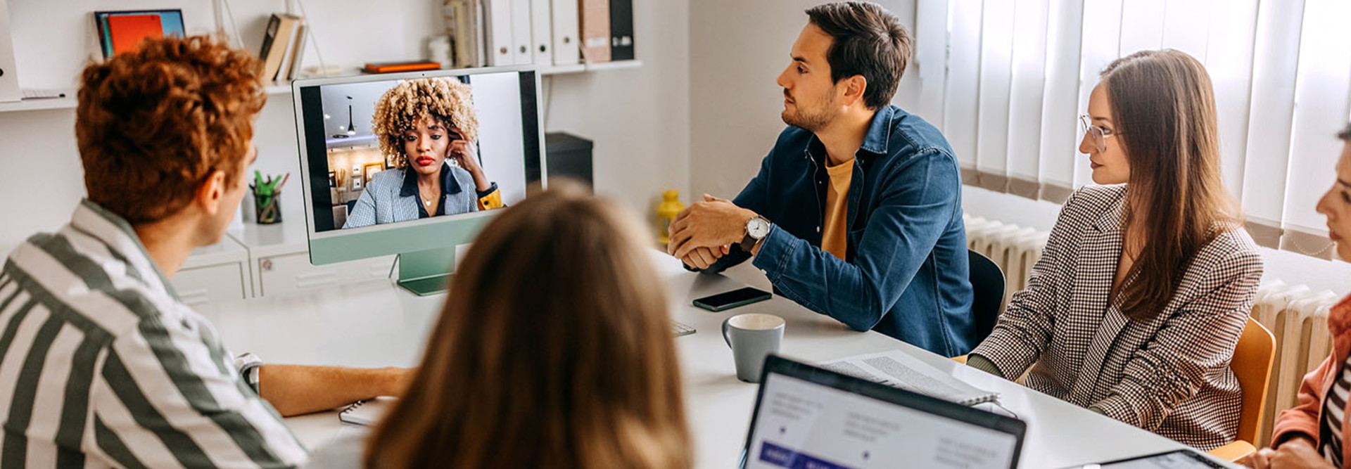 Image of in-person workers in a conference room holding a video call with remote workers.