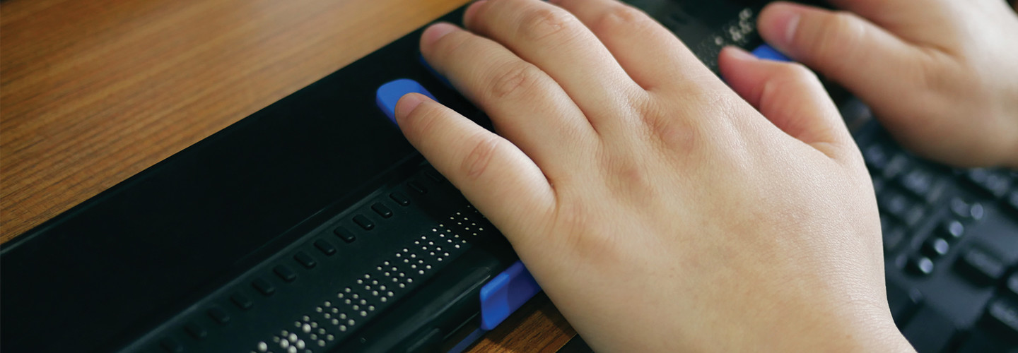 Close-up blind person hands using computer with braille display or braille terminal a technology assistive device for persons with visual disabilities.