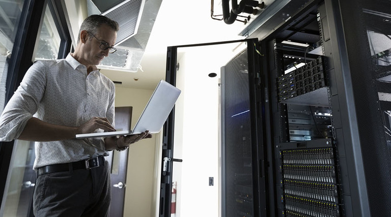 Male Caucasian IT technician using laptop in server room