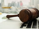 Wooden gavel on laptop keyboard with scales of justice in business city background.