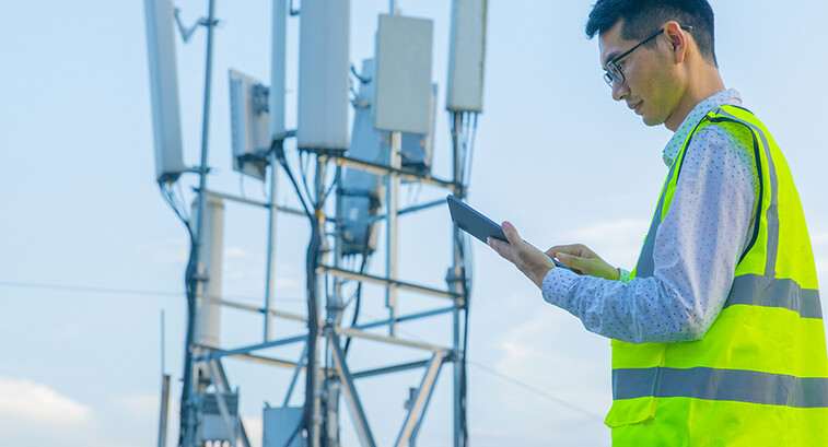 Engineer working on a digital tablet near communications tower