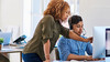Female worker directing young intern on computer